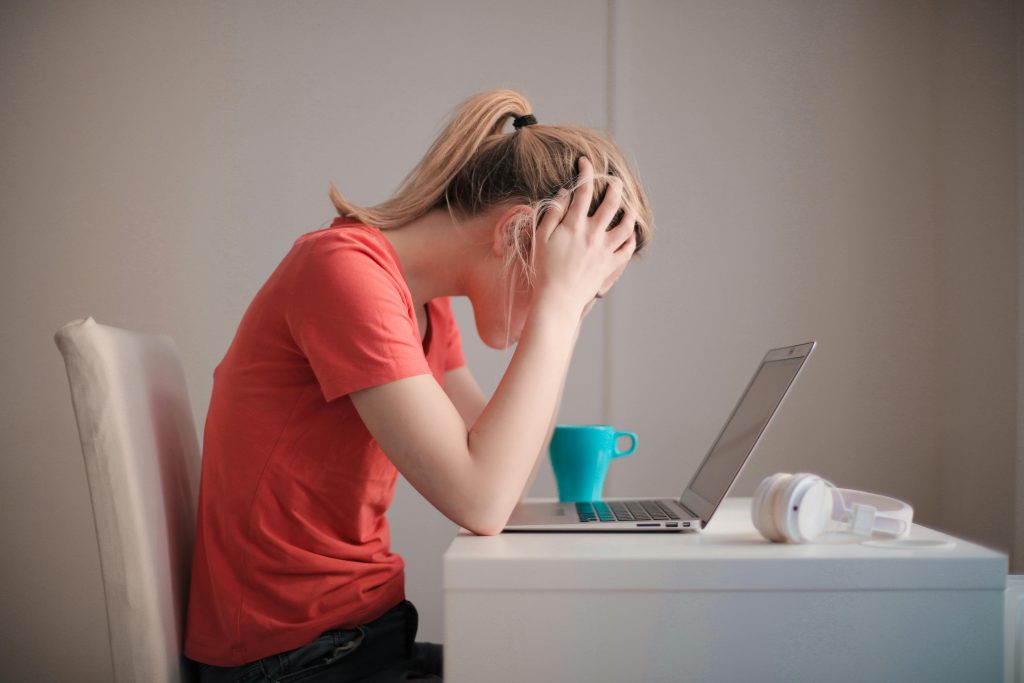 A lady sitting at the computer with her head in her hands.